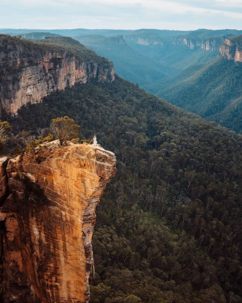 A lone figure stands on the edge of Hanging Rock, a dramatic sandstone outcrop jutting over a deep valley—this hike is a thrilling thing to do in the Blue Mountains.