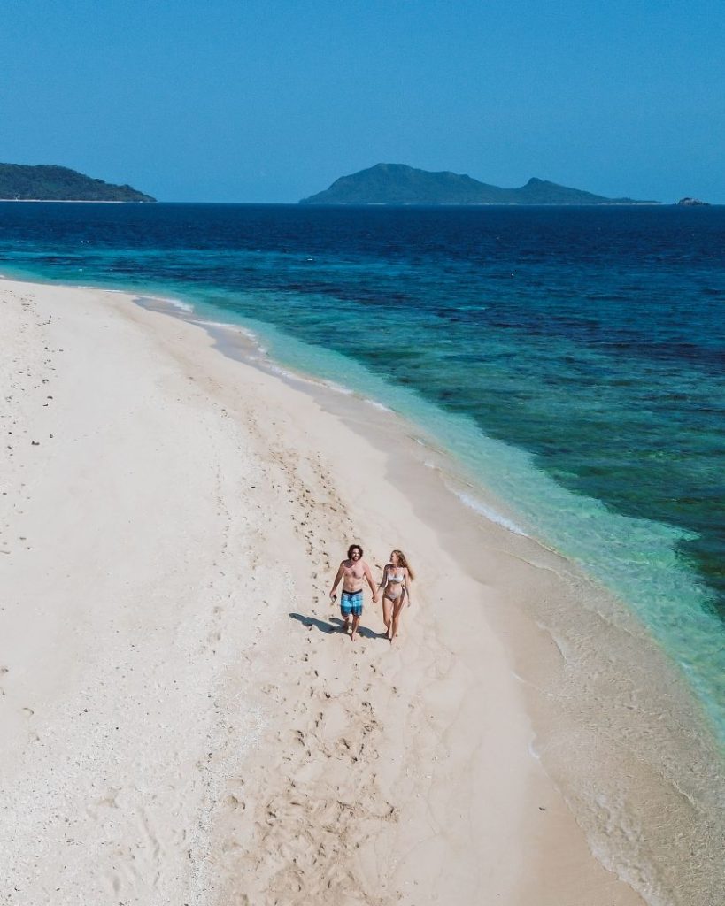 Couple walking on a deserted beach with white sand and blue water, a peaceful scene often found in the Philippines during the best travel months.