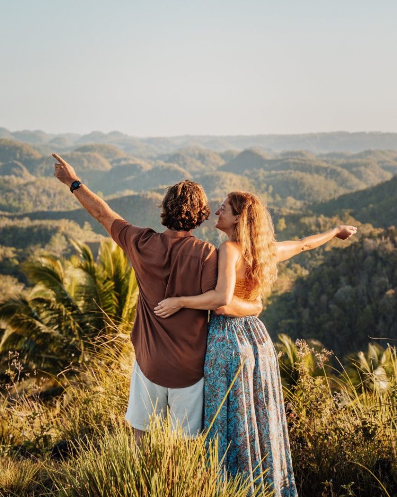 A couple stands atop a hill, embracing as they look out over the rolling landscape of Bohol, Philippines. One of the most scenic places to visit in the Philippines, known for its lush countryside and natural wonders.