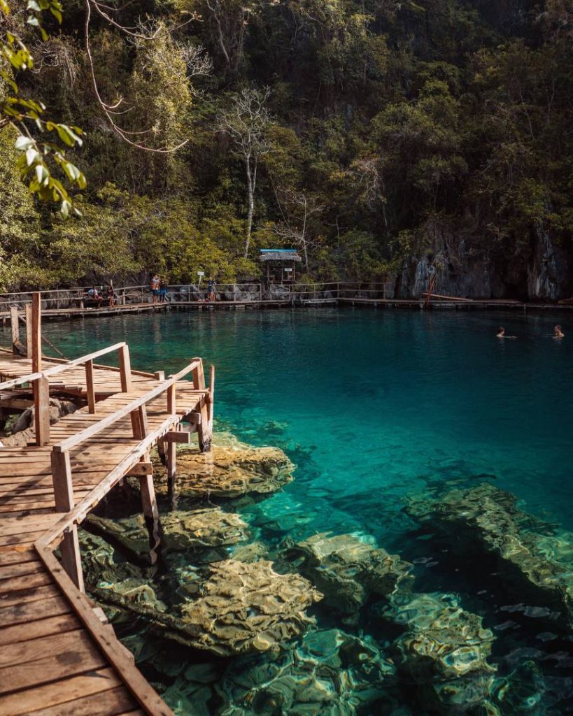 A scenic view of Kayangan Lake with a wooden dock extending into the crystal-clear water, surrounded by limestone cliffs, proving that nature’s wonders come at a low Philippines travel cost.