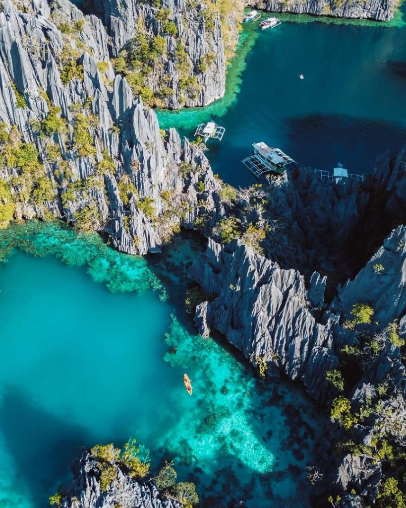 Aerial view of the Twin Lagoon in Coron, featuring stunning turquoise waters, dramatic limestone cliffs, and traditional boats, demonstrating the affordable cost of traveling the Philippines.