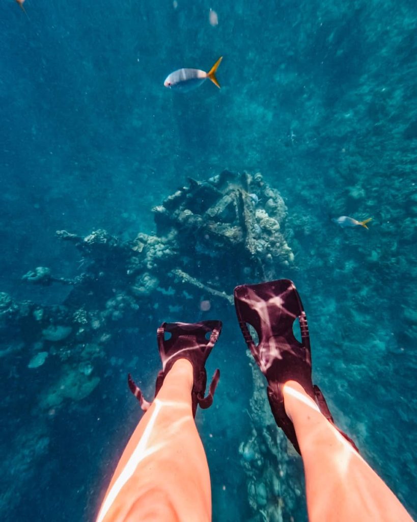 A snorkeller’s fins hover above a sunken shipwreck and coral reef, with tropical fish swimming by—an epic underwater moment from the best snorkelling tours in Coron.