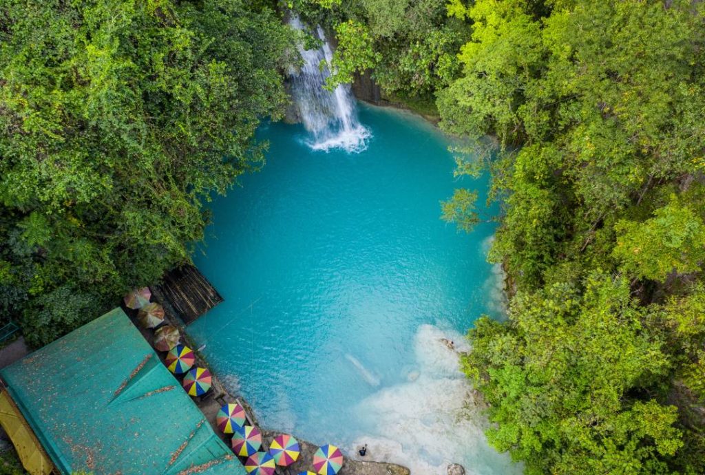Aerial view of Kawasan Falls in Cebu, Philippines, with its stunning turquoise pool surrounded by lush greenery and a cascading waterfall. A must-visit spot in the Philippines, famous for its canyoneering and natural beauty.