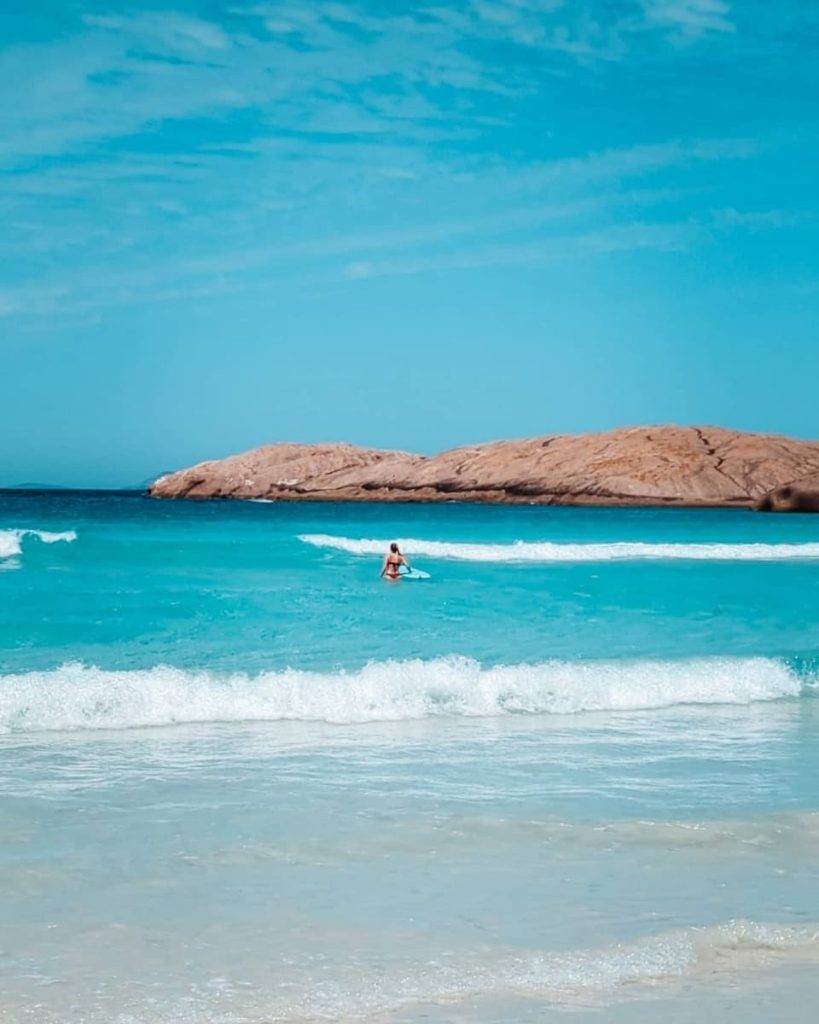 A lone swimmer on a paddleboard floats in the aqua waters of Wharton Beach in Esperance, a serene stop for road trips in Australia’s southwest.