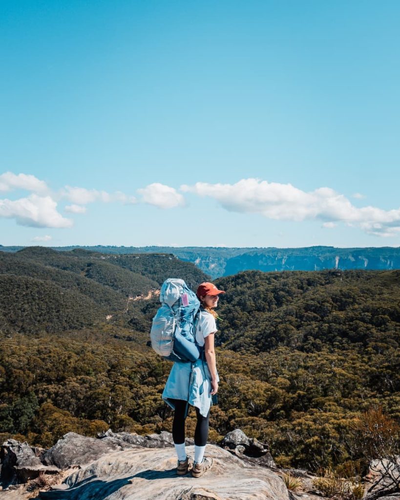 A solo hiker with a large backpack gazes across rolling forested ridges from Lockleys Pylon, a scenic lookout included in many Blue Mountains weekend hiking plans.