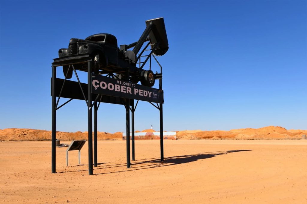 The quirky Coober Pedy entrance sign featuring a mining blower on stilts, set against a red desert backdrop—outback charm on epic road trips in Australia.