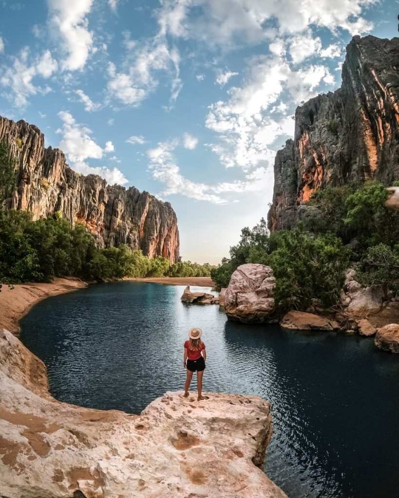 A woman stands at the edge of Windjana Gorge in Western Australia, surrounded by towering cliffs and a calm river—raw beauty on Gibb River road trips in Australia.