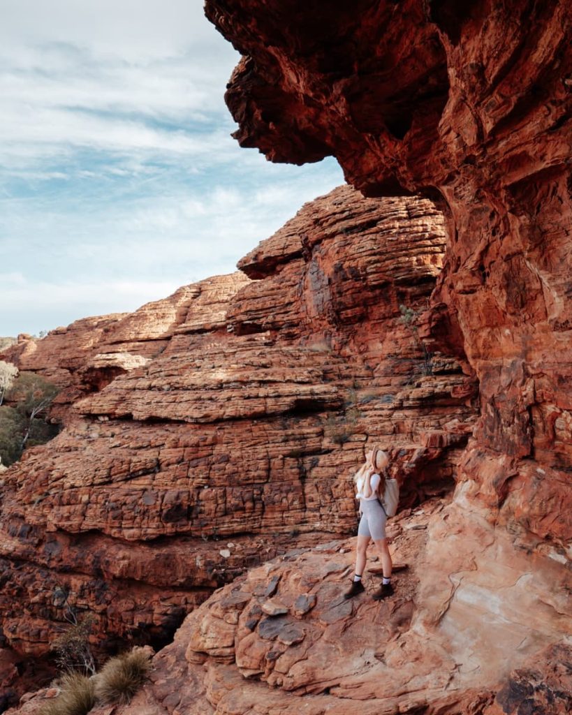 A hiker explores the weathered red rock walls of Kings Canyon in the Northern Territory, a dramatic detour for adventurous road trips in Australia.