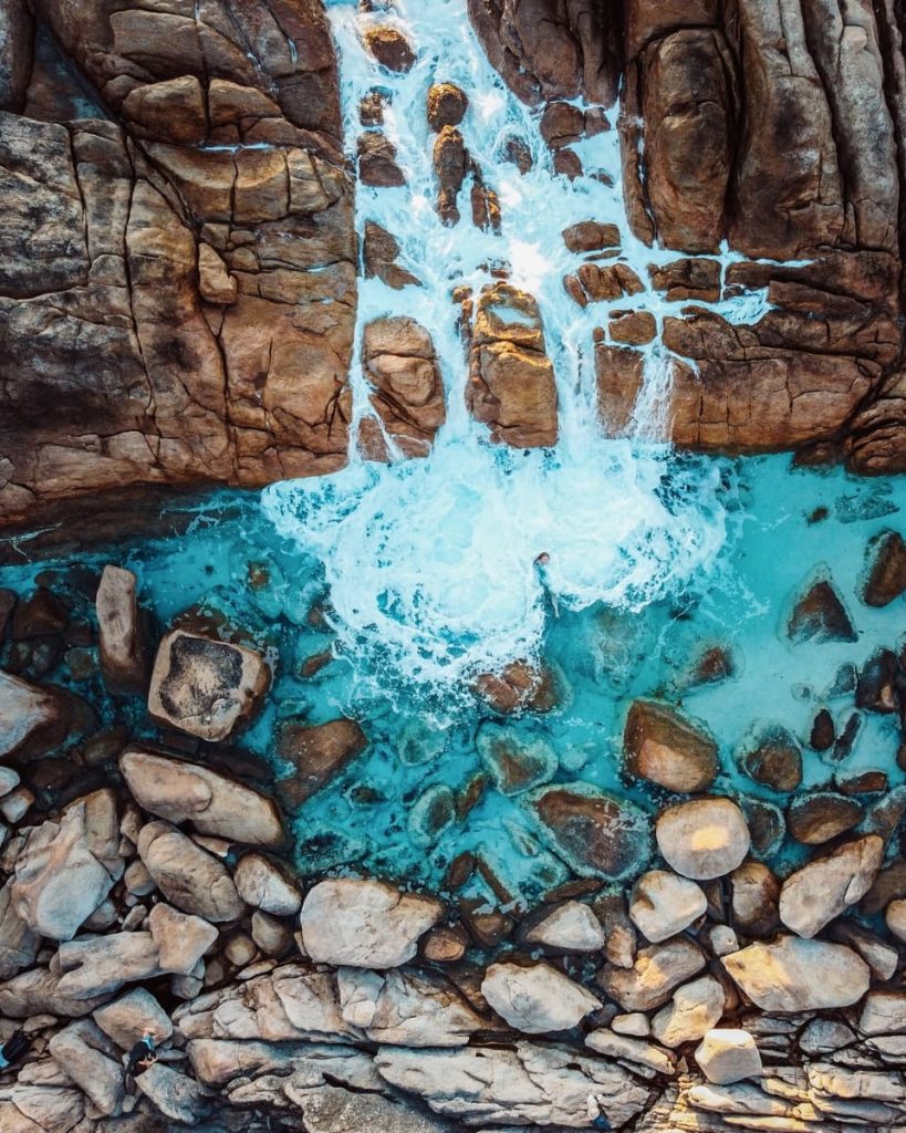 Aerial view of waves crashing through rock crevices into the turquoise waters of Injidup Natural Spa near Yallingup, a must-see coastal spot on road trips in Australia.