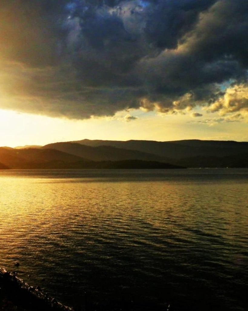 A dramatic sunset over the water with dark clouds and silhouetted hills, captured from the ferry to Bruny Island in Tasmania, a picturesque moment on road trips around Australia.