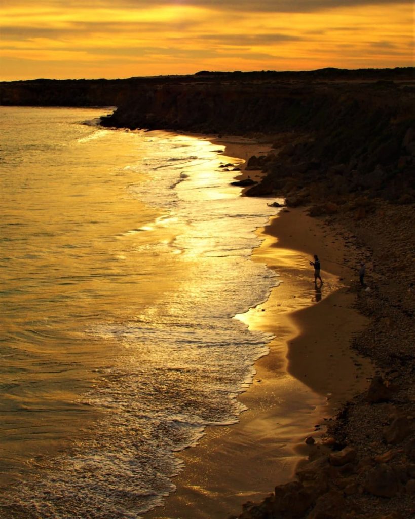 Golden sunset reflecting along the shoreline with silhouetted figures at the water’s edge in Yorke Peninsula—perfect for slow, peaceful road trips in Australia.