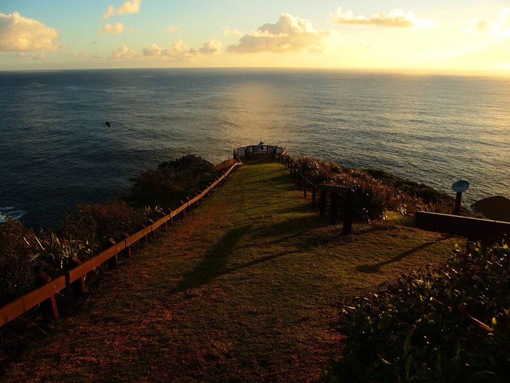 Wooden-fenced path leading to Captain Cook Lookout on Norfolk Island, glowing in golden early morning light with ocean views stretching to the horizon.