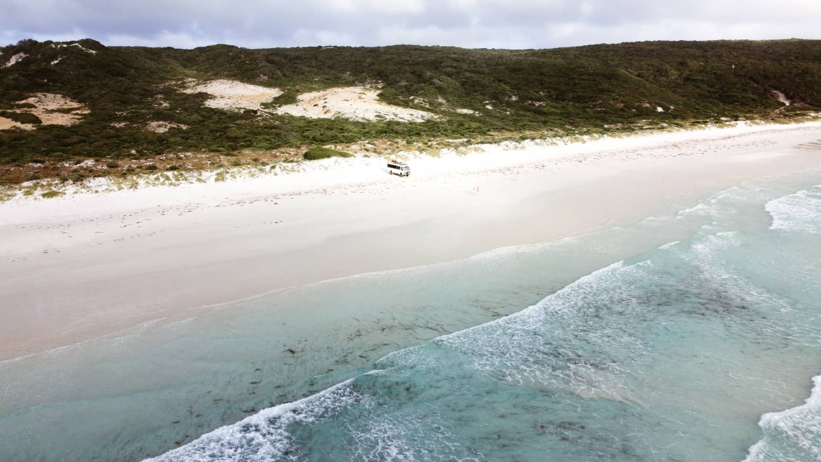 A campervan parked on a remote, pristine beach with white sand and turquoise water, surrounded by dense green dunes—captured along a scenic Perth to Bremer Bay road trip.
