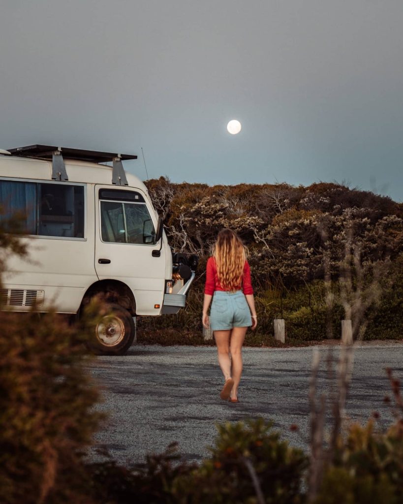 A woman walks barefoot toward a camper van under a full moon in Albany, capturing the magic of evenings on a Perth to Bremer Bay road trip.