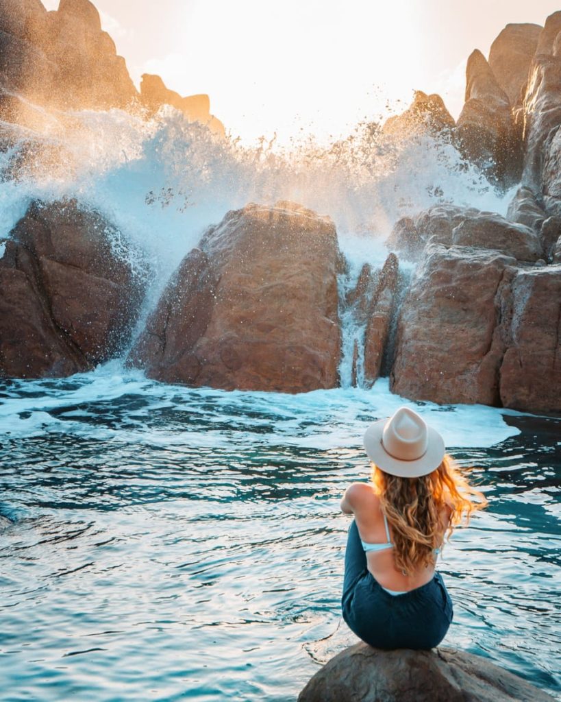 Woman sitting on a rock watching waves crash dramatically at Injidup Natural Spa in Yallingup, a must-visit natural wonder on the Perth to Albany road trip route.