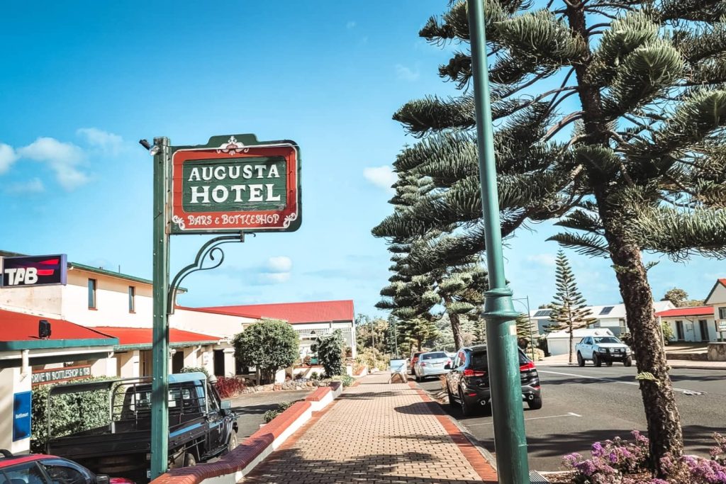The vintage-style Augusta Hotel sign in the town centre, with Norfolk pines lining the street—a classic stop on a Perth to Albany road trip itinerary.
