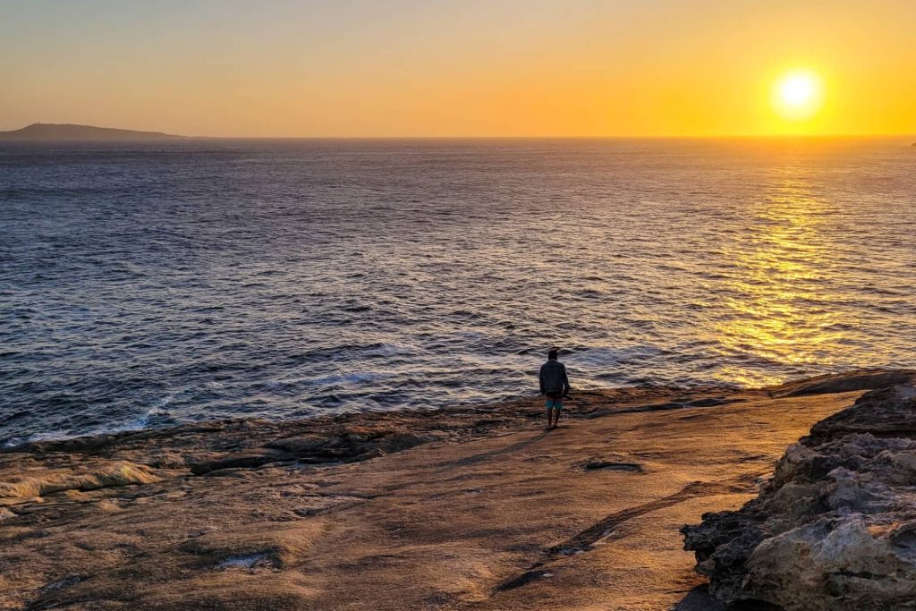 A person stands on a rocky headland at Albany watching the sun set over the ocean, a serene stop on the Perth to Bremer Bay road trip.