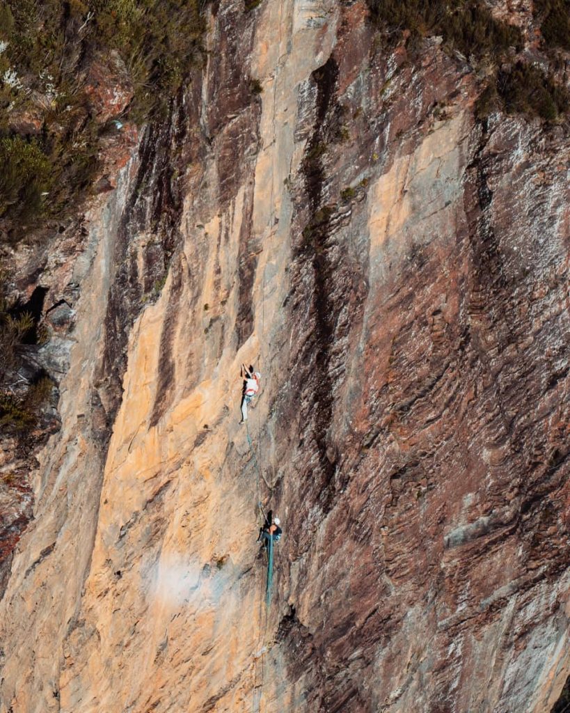 Two people abseiling down a sheer rock face in the Blue Mountains, suspended by ropes against the rugged cliff wall.