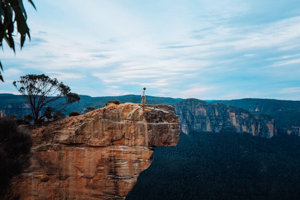 Person standing on the edge of Hanging Rock, a dramatic sandstone outcrop jutting over the forested valley in the Blue Mountains, NSW.