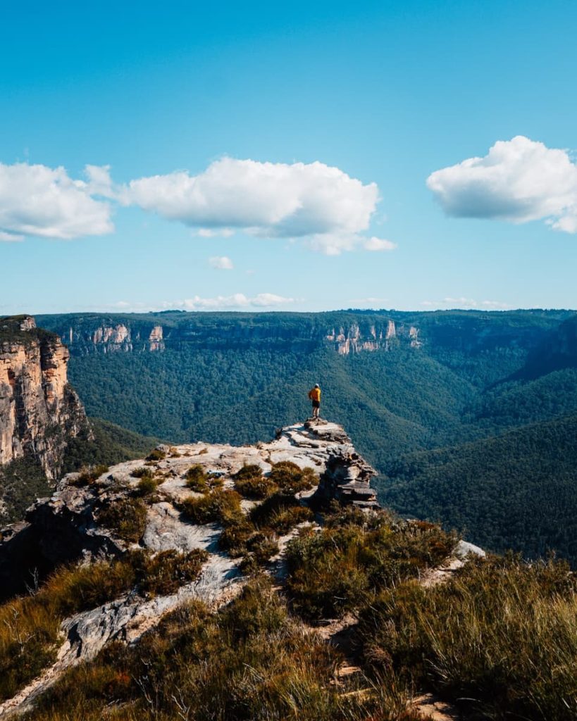 Hiker standing on the rocky outcrop of Lockleys Pylon overlooking forested valleys and sandstone cliffs in the Blue Mountains, NSW.