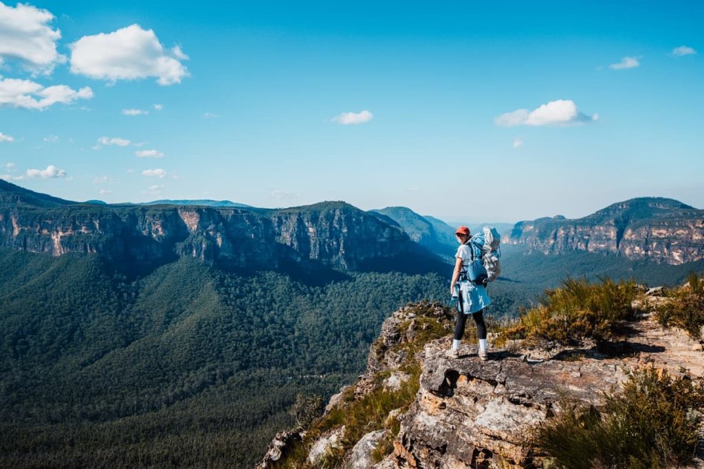 Hiker standing on the edge of Lockleys Pylon, looking over a deep valley and surrounding sandstone cliffs in the Blue Mountains, NSW.