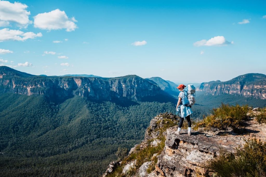 Hiker standing on a rocky outcrop at Lockleys Pylon, overlooking sweeping forested valleys and cliffs in the Blue Mountains, NSW.