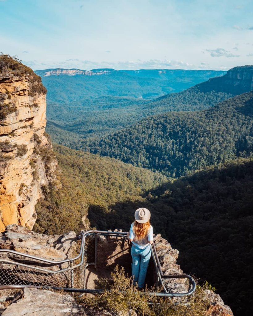 Woman standing at Rocket Point Lookout above Wentworth Falls, gazing across deep forested valleys and distant cliffs in the Blue Mountains, NSW.