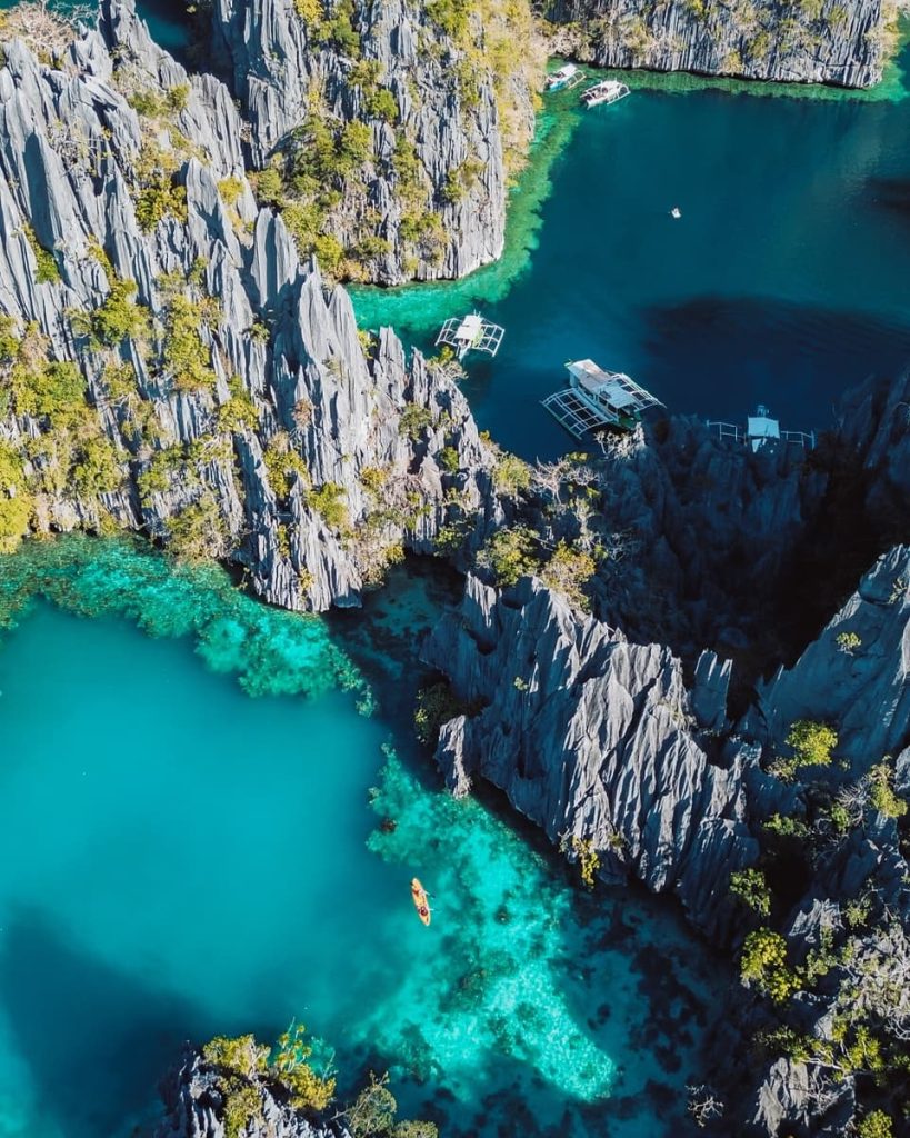 Aerial view of limestone cliffs and turquoise waters at Twin Lagoon, with a kayak paddling through—one of the top things to do in Coron, Philippines.